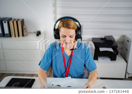Woman wearing scrubs and headset providing online medical consultation 137261448