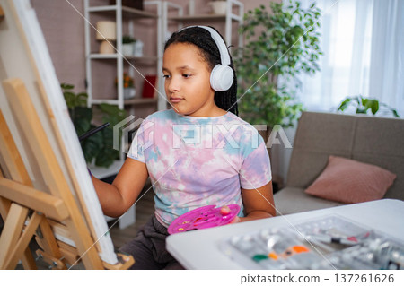 Young girl wearing headphones painting art on canvas at home Young girl wearing headphones painting art on canvas at home 137261626