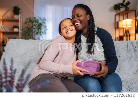Mother and daughter celebrating giving gift on sofa Mother and daughter celebrating giving gift on sofa 137261638