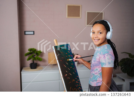 Smiling girl wearing headphones painting on canvas while learning Smiling girl wearing headphones painting on canvas while learning 137261643