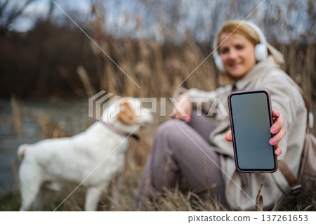 Woman holding smartphone mockup with dog in nature 137261653