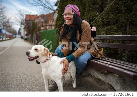 Happy black woman petting dog on park bench 137261661