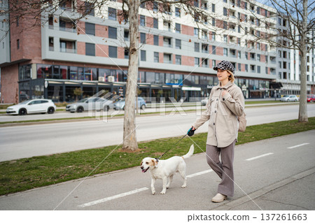 Woman walking her dog on an city sidewalk 137261663