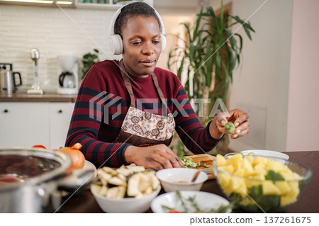 Woman wearing headphones preparing healthy vegetables in kitchen 137261675