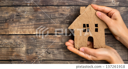 Hands holding a brown house shape on a rustic wooden table for home concept Hands holding a brown house shape on a rustic wooden table for home concept 137261918