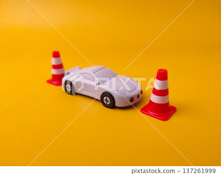 Toy sports car positioned next to three miniature red and white traffic cones on a yellow surface. Toy sports car positioned next to three miniature red and white traffic cones on a yellow surface. 137261999