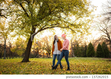 Diverse women friends walking in autumn park 137262015