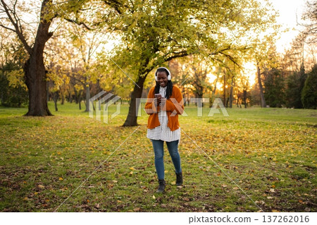 Young woman enjoying music on headphones in autumn park Young woman enjoying music on headphones in autumn park 137262016