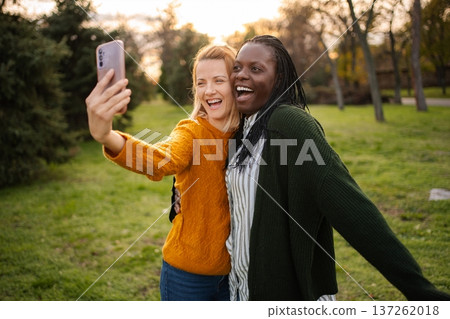 Diverse women friends taking selfie in park, laughing happily 137262018