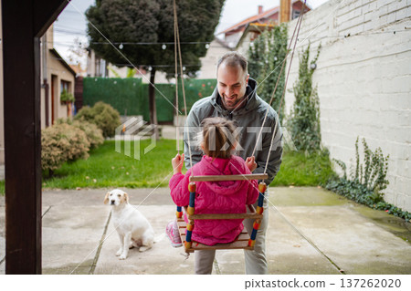 Father pushing daughter on swing in backyard with dog 137262020