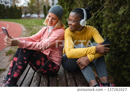 Diverse women friends resting on bench using smartphone 137262027