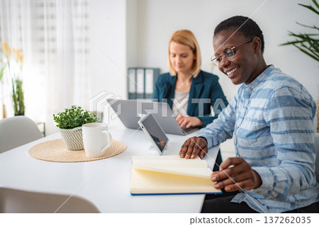 Two diverse businesswomen smiling and working together at a desk 137262035
