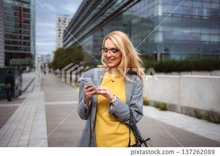 Young adult businesswoman using smartphone walking city street Young adult businesswoman using smartphone walking city street 137262089