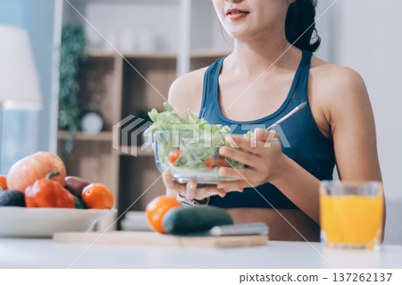 Fit young Asian women in activewear sitting on yoga mat and eating fresh vegetable salad after workout, representing clean eating, fitness lifestyle, wellness routine and health balance. Fit young Asian women in activewear sitting on yoga mat and eating fresh vegetable salad after workout, representing clean eating, fitness lifestyle, wellness routine and health balance. 137262137