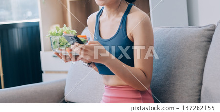Fit young Asian women in activewear sitting on yoga mat and eating fresh vegetable salad after workout, representing clean eating, fitness lifestyle, wellness routine and health balance. Fit young Asian women in activewear sitting on yoga mat and eating fresh vegetable salad after workout, representing clean eating, fitness lifestyle, wellness routine and health balance. 137262155