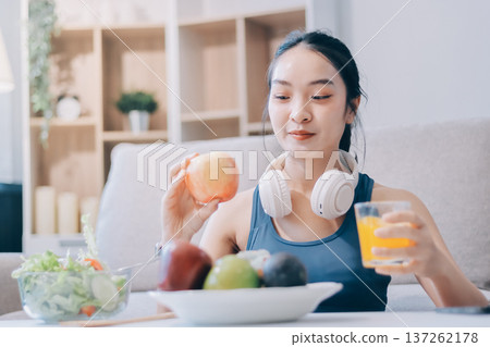 Fit young Asian women in activewear sitting on yoga mat and eating fresh vegetable salad after workout, representing clean eating, fitness lifestyle, wellness routine and health balance. 137262178