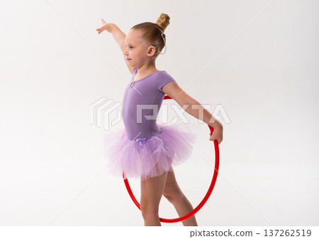 Young dancer with a cochlear implant balances with a red hoop during studio training. Inclusive performance, auditory support, and physical development through rhythmic gymnastics and ballet. Young dancer with a cochlear implant balances with a red hoop during studio training. Inclusive performance, auditory support, and physical development through rhythmic gymnastics and ballet. 137262519