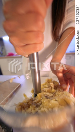 Person prepares mashed potatoes using wooden spoon in home kitchen setting 137262524