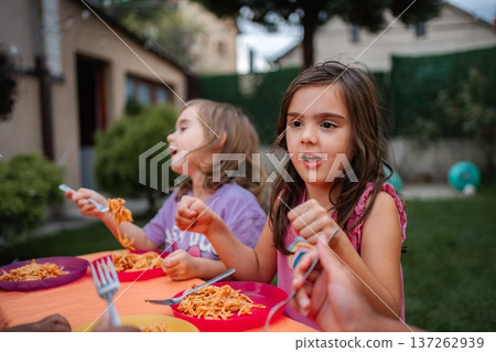 Children eating pasta outdoors during backyard summer dinner 137262939