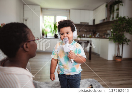 Little boy performing karaoke at home while mother is watching him Little boy performing karaoke at home while mother is watching him 137262943