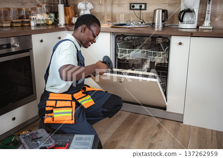 Technician repairing dishwasher using electric screwdriver in kitchen Technician repairing dishwasher using electric screwdriver in kitchen 137262959