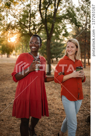 Two smiling friends walking and talking in a park at sunset Two smiling friends walking and talking in a park at sunset 137263167
