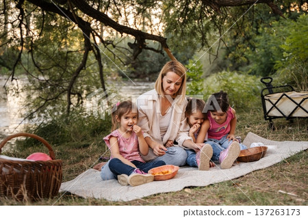Mother enjoying picnic by the river with her three daughters 137263173