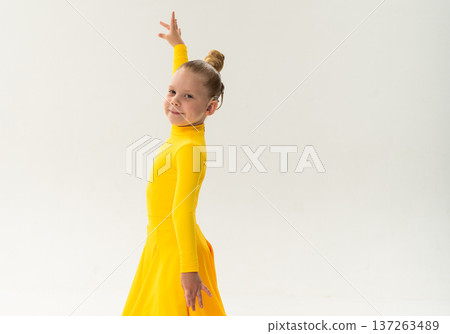 Young ballroom dancer with cochlear implant in yellow dress posing in studio. Copy space. Pediatric hearing rehabilitation, dance therapy and inclusive performance through movement and balance Young ballroom dancer with cochlear implant in yellow dress posing in studio. Copy space. Pediatric hearing rehabilitation, dance therapy and inclusive performance through movement and balance 137263489