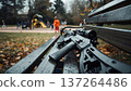 A rifle lying on a park bench, against a blurred backdrop of a playground and children. Conceptualizing gun control, public safety, and social risks. 137264486