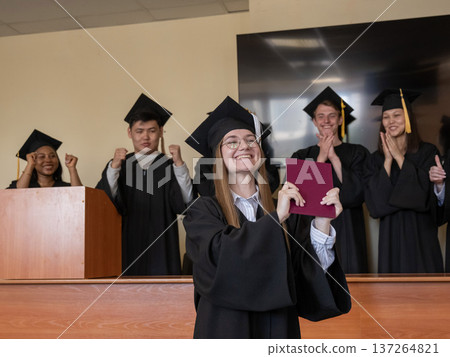 Happy Caucasian woman holds red diploma and classmates support her.  137264821