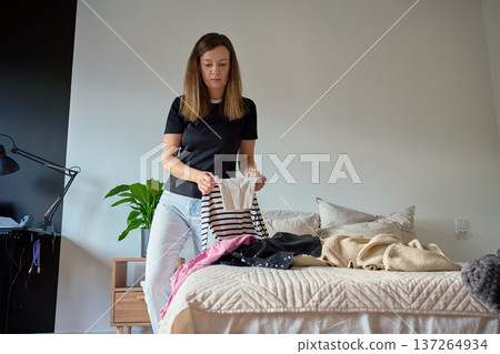 Woman packing clothes into suitcase in bright bedroom Woman packing clothes into suitcase in bright bedroom 137264934