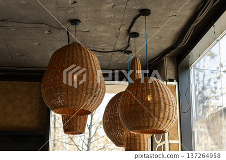 Woven straw lampshades hanging from concrete ceiling near window, modern rustic interior design. 137264958