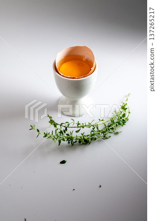 Fresh egg cracked open with bright yellow yolk, served in white ceramic egg cup on clean white background. Fresh egg cracked open with bright yellow yolk, served in white ceramic egg cup on clean white background. 137265217
