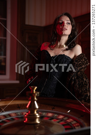 A beautiful brunette in a black dress at the casino roulette wheel.  137265271