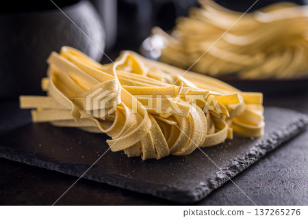 Fresh pasta ready for cooking, showing strands of fettuccine set on a black table. Fresh pasta ready for cooking, showing strands of fettuccine set on a black table. 137265276