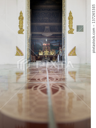 At Wat Phong Sunan, a striking marble perspective draws the gaze past golden sculptures into a hidden sanctuary, revealing a serene Buddha seated beneath a delicate chandelier. 137265385