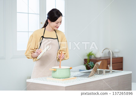 A housewife cooking while looking at a computer in the kitchen A housewife cooking while looking at a computer in the kitchen 137265896