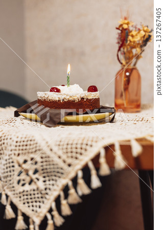 Chocolate birthday cake with a burning candle on a lace tablecloth in a moody vintage interior. Festive still life for holiday and celebration designs Chocolate birthday cake with a burning candle on a lace tablecloth in a moody vintage interior. Festive still life for holiday and celebration designs 137267405