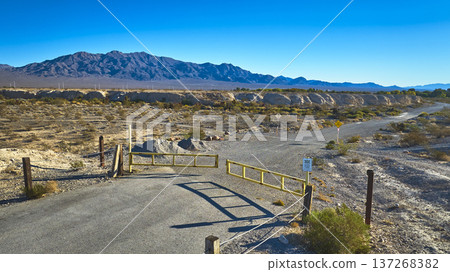 Nevada Desert Road Gate and Mountain Range with Shadow Under Blue Sky Nevada Desert Road Gate and Mountain Range with Shadow Under Blue Sky 137268382