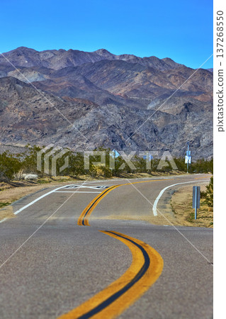 Winding Mojave Desert Road and Rugged Mountains Under Clear Blue Sky California Winding Mojave Desert Road and Rugged Mountains Under Clear Blue Sky California 137268550