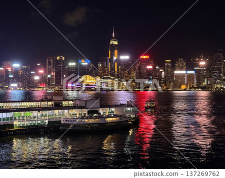 Hong Kong skyline at night with ferries and illuminated skyscrapers reflecting on the water 137269762