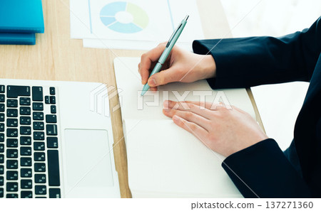 Businesswoman taking notes at her desk 137271360