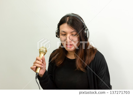 Woman wearing headphones holding microphone singing in studio isolated on white background music recording and vocal performance concept Woman wearing headphones holding microphone singing in studio isolated on white background music recording and vocal performance concept 137271703