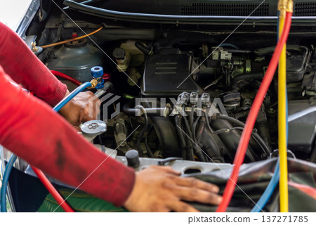 Mechanic checking car air conditioning system with manifold gauge set under open hood during vehicle maintenance repair in auto service garage close up engine bay work Mechanic checking car air conditioning system with manifold gauge set under open hood during vehicle maintenance repair in auto service garage close up engine bay work 137271785