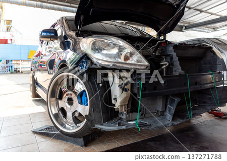 Black car with front bumper removed and hood open during maintenance in auto repair garage showing engine components wheel and mechanical service process Black car with front bumper removed and hood open during maintenance in auto repair garage showing engine components wheel and mechanical service process 137271788
