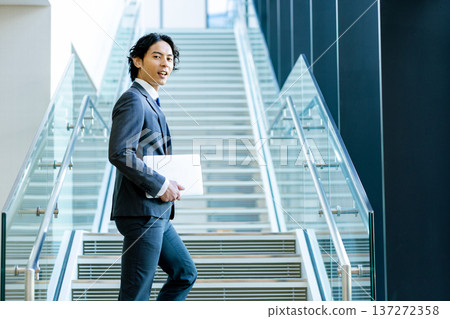 A young businessman in a suit walking down the stairs in the office A young businessman in a suit walking down the stairs in the office 137272358