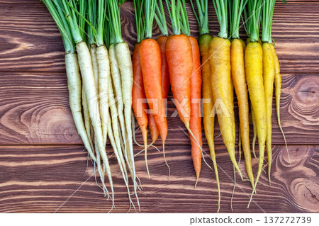Yellow, orange and white carrots on the brown wooden table. Yellow, orange and white carrots on the brown wooden table. 137272739