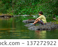 Teen boy sits on a big rock in the mountain river. 137272922