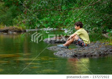 Teen boy sits on a big rock in the mountain river. 137272922
