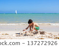 Teen boy is playing with white sand at the tropical beach. 137272926